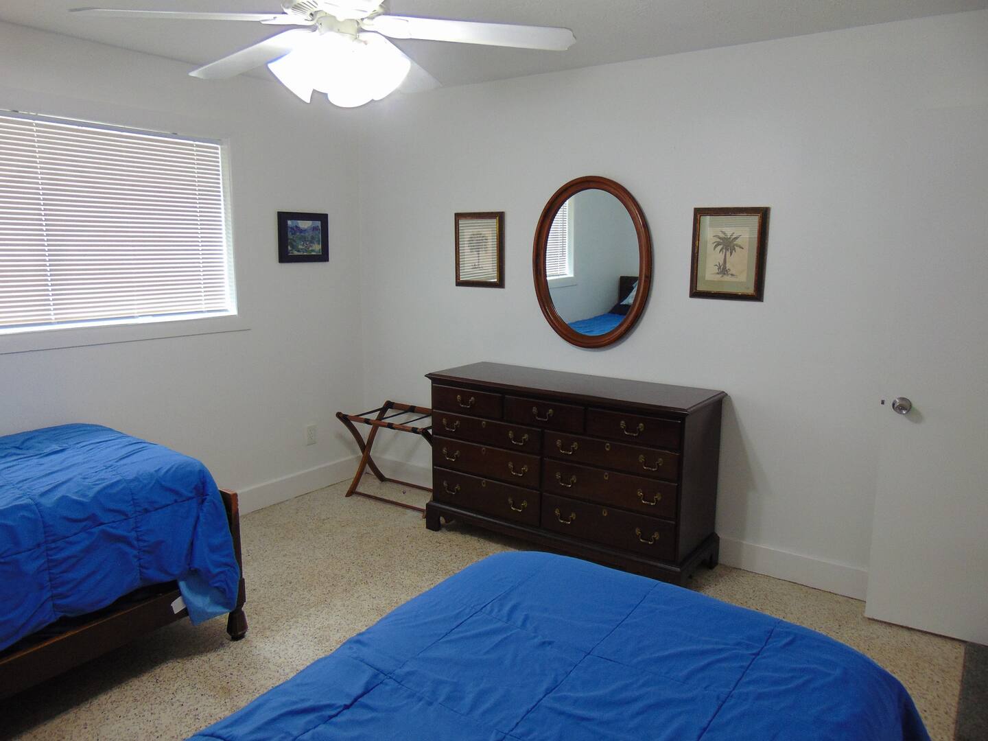 Your comfortable bedroom features two beds with cheerful blue linens, a classic dresser with mirror, and a ceiling fan to keep you cool during your stay.