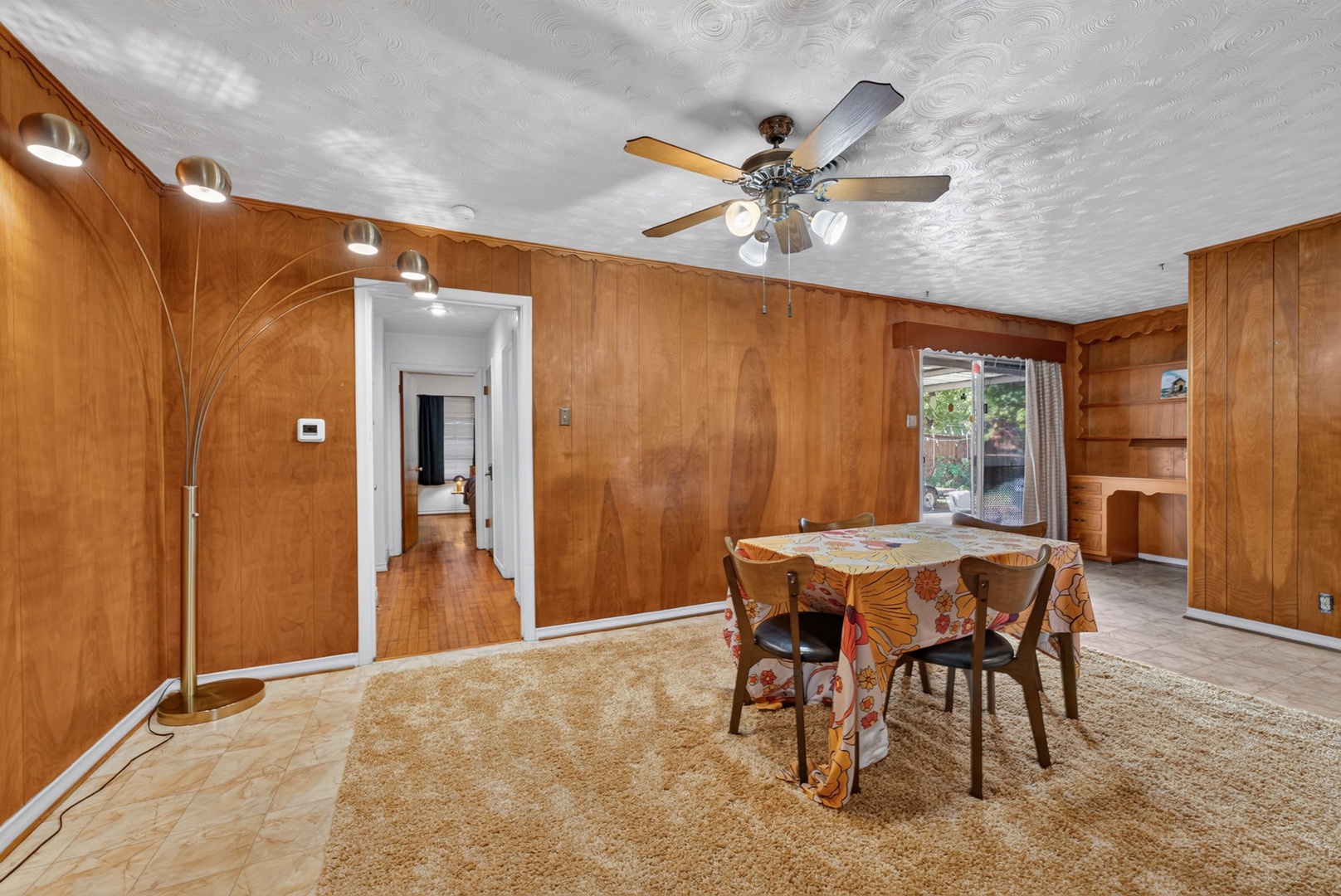 Step into your spacious dining room, wrapped in warm wood paneling with a stylish ceiling fan to keep you comfortable. The table is ready for shared meals, and natural light spills in from sliding doors leading to your private outdoor space.