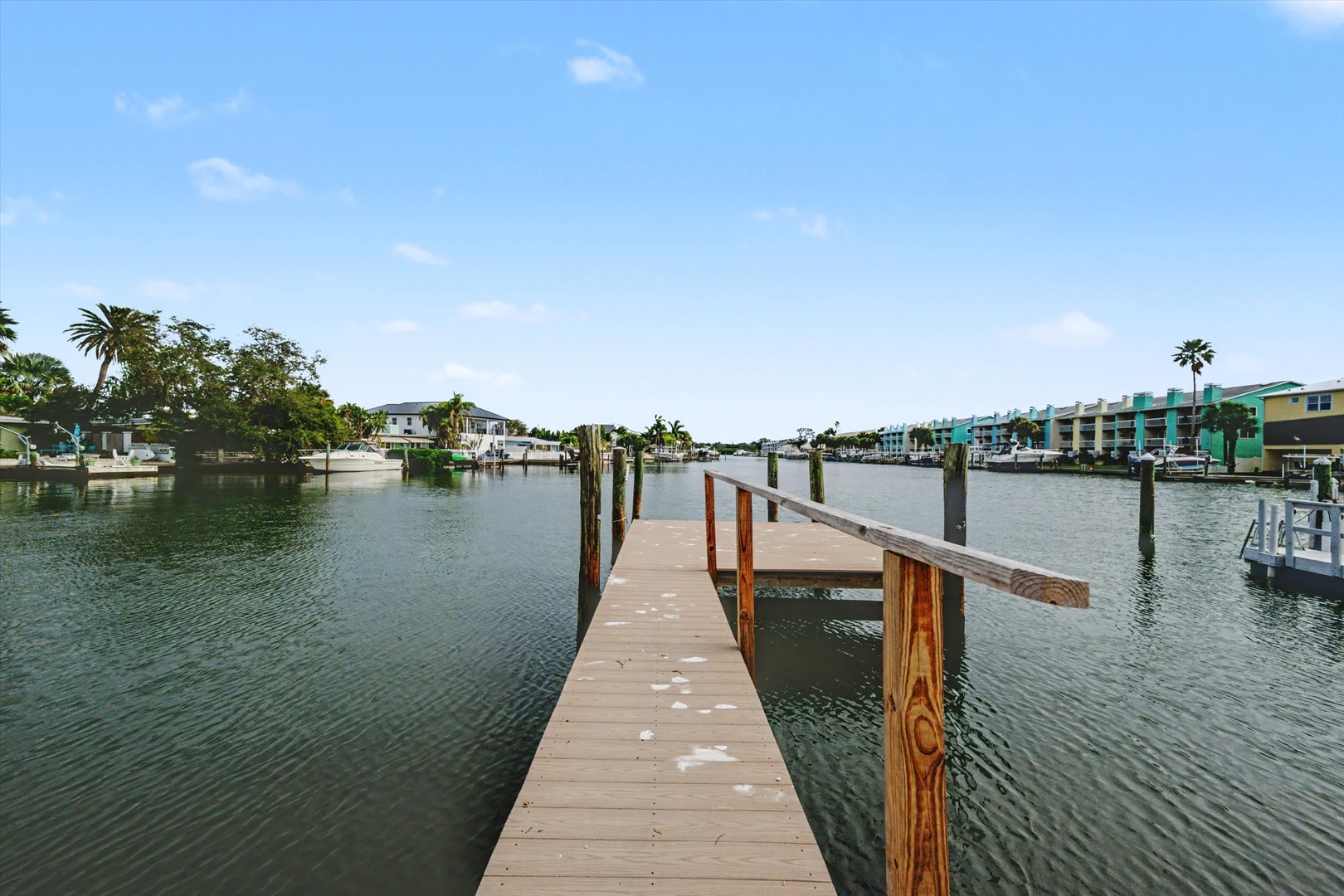 A private dock extends into calm canal waters, lined with waterfront homes and swaying palms under a sunny Florida sky.