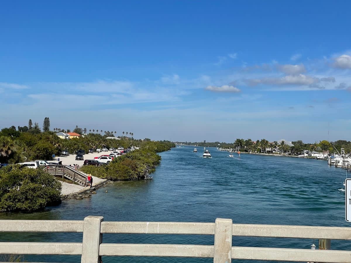 A tranquil waterway winds through the neighborhood, lined with swaying palms and dotted with boats gently floating by—a scenic slice of coastal living just steps from the property.
