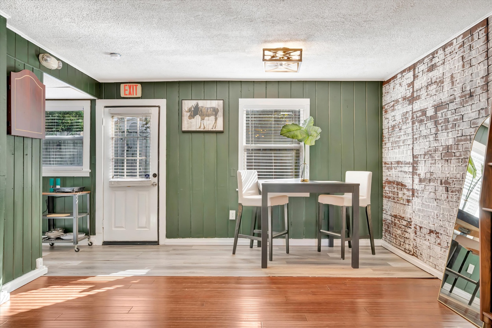 Gather around the rustic high-top table in this cozy dining nook, where rich green paneling and exposed brick create an inviting farmhouse atmosphere perfect for morning coffee or evening meals.