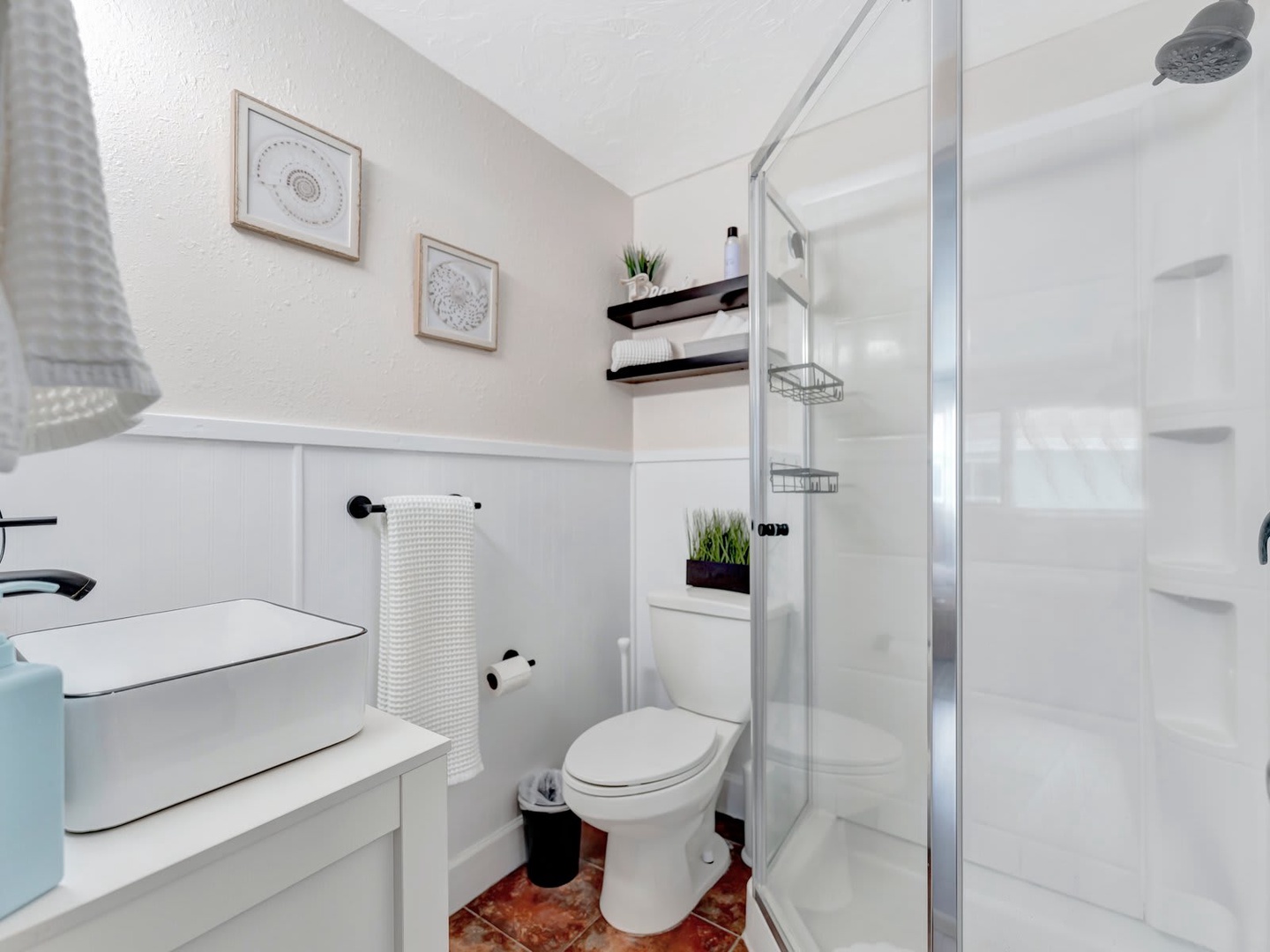 Step into your private bathroom, where a sparkling walk-in shower and crisp white towels await. The thoughtful touches—floating shelves, fresh greenery, and peaceful artwork—create a serene retreat for your morning routine.