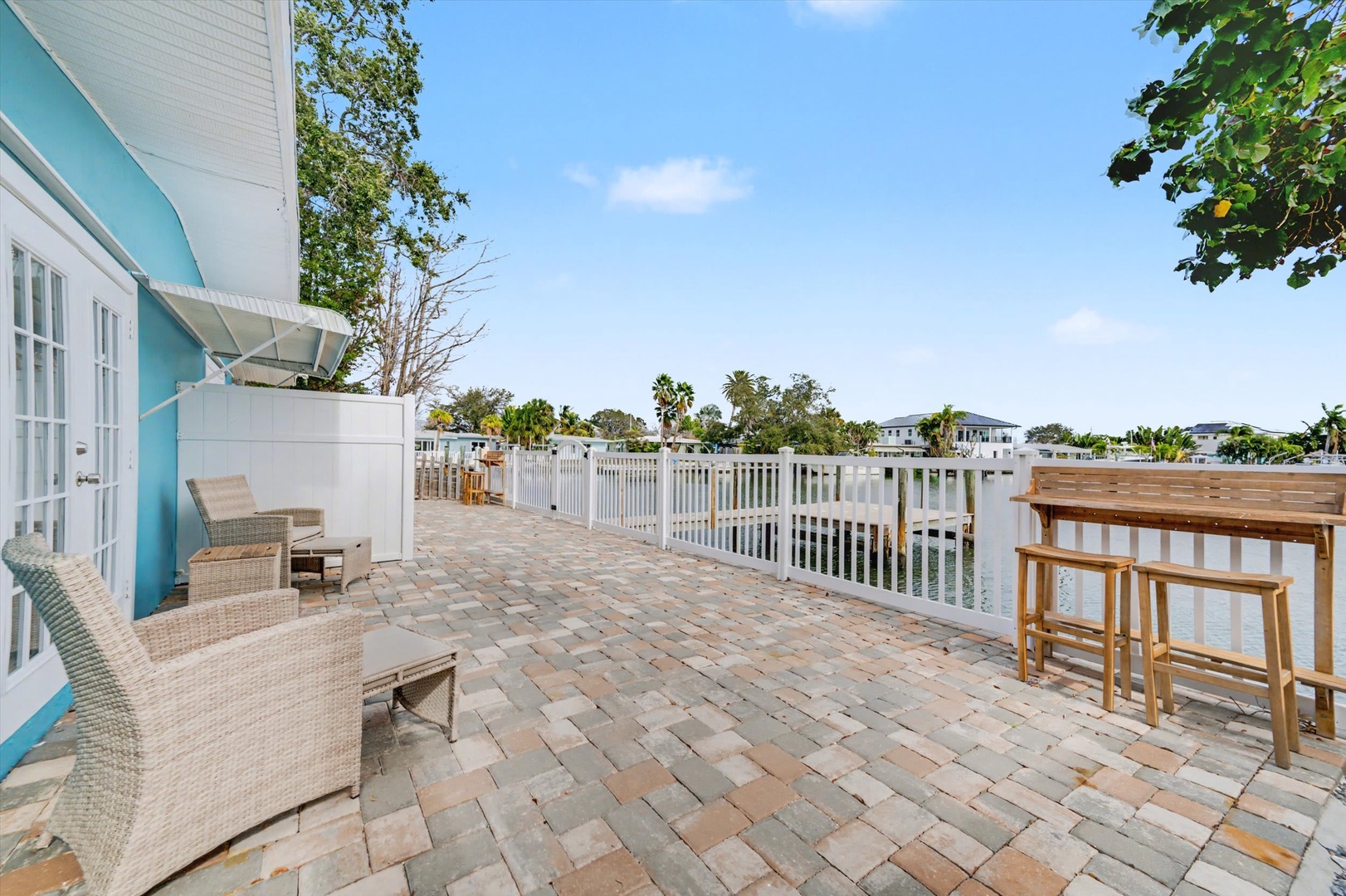 This spacious waterfront deck offers plenty of room to relax in comfortable seating or gather at the bar-height table, all framed by tropical palms and bright coastal skies.