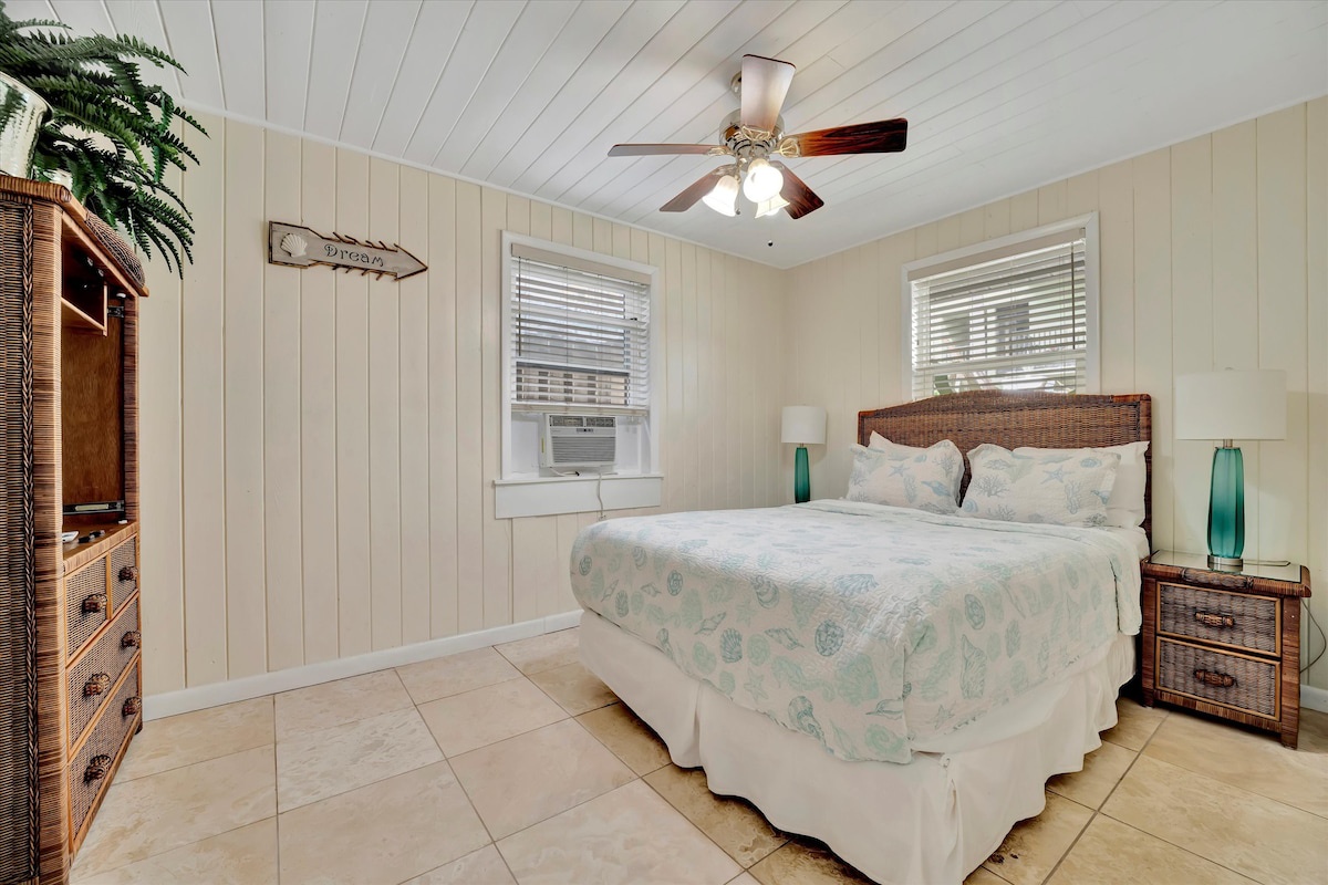 Slip into your coastal retreat and unwind beneath the gentle ceiling fan. Wicker accents and soft linens in soothing pastels invite you to relax after a day exploring the shore.