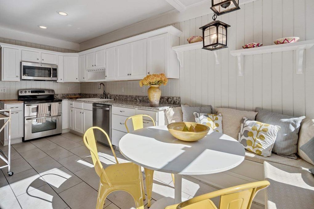 Your cottage-style kitchen and dining nook blend seamlessly—bright white cabinetry, modern appliances, and cozy seating invite lazy morning coffees or casual meals in the cheerful yellow accents of coastal charm.