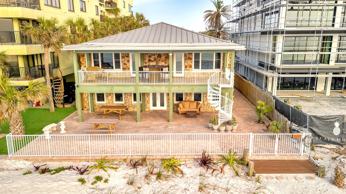 A charming elevated coastal property surrounded by palm trees, featuring spacious covered patios and direct beach access through private sandy grounds.