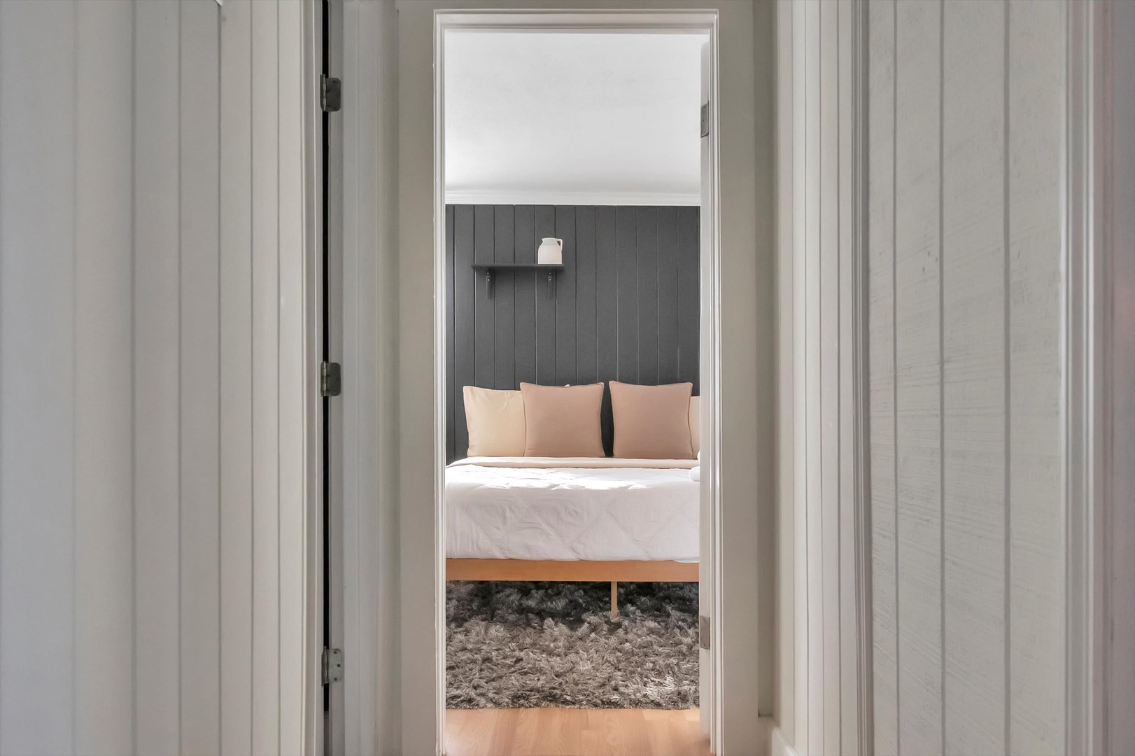Step through the doorway into your serene bedroom retreat, where a plush bed awaits beneath a modern dark grey accent wall.