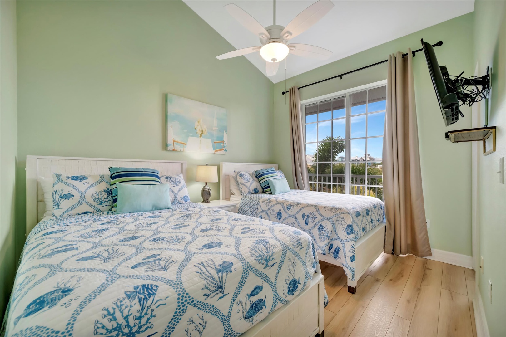 Your coastal-inspired retreat features twin beds dressed in soothing ocean blues, where soft breezes from the ceiling fan and natural light create a perfectly serene sleeping space.