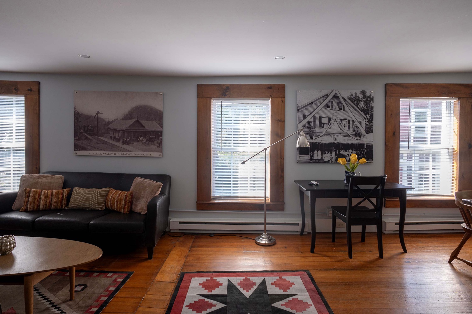 Bright, welcoming living space featuring rich wood floors, vintage photography, leather sofa, and work desk by the window with natural light.