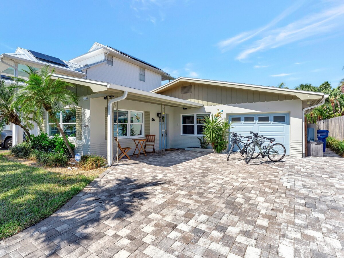 A charming coastal-style home with a spacious paver driveway, lush tropical landscaping, and covered entry—perfect for your beach retreat. Bicycles ready for exploring the area.