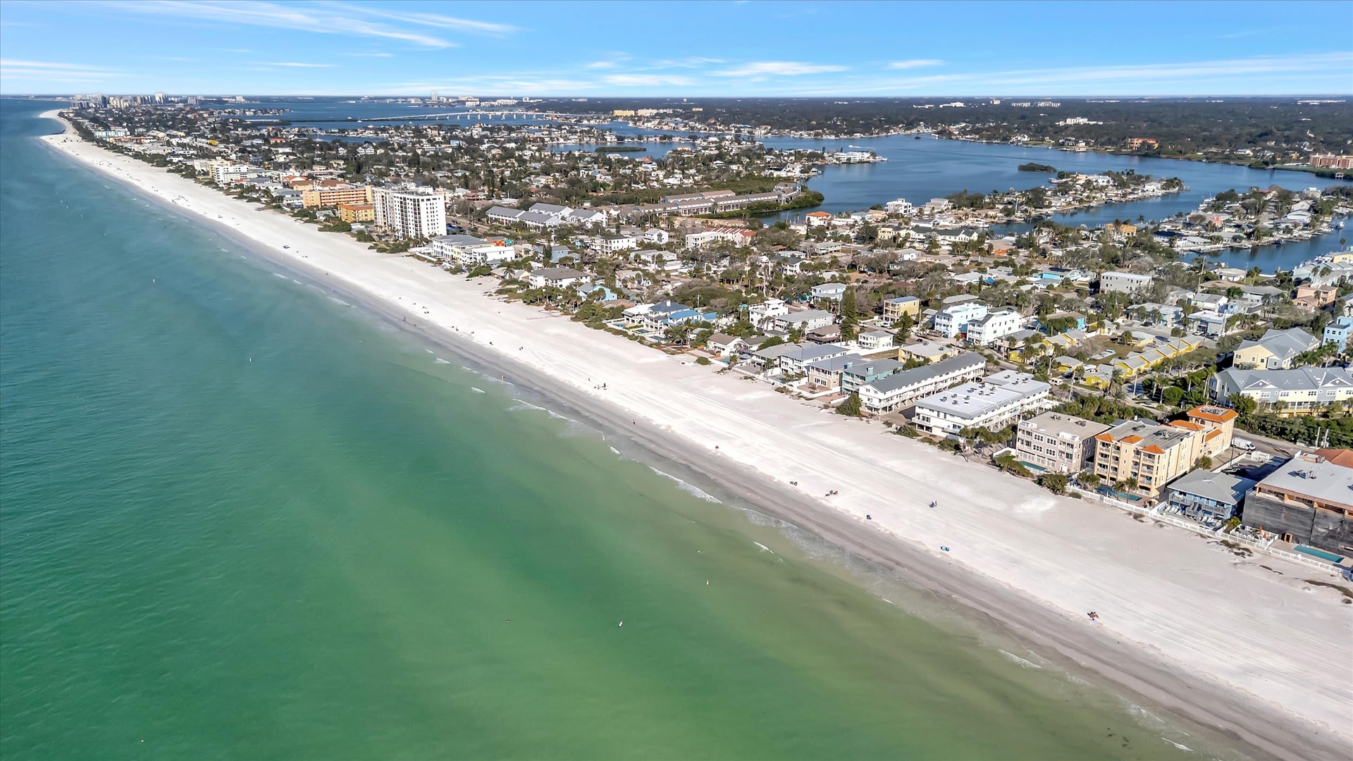 Aerial view of a coastal area with pristine white sand beach, turquoise waters, and waterfront neighborhoods along inland waterways.