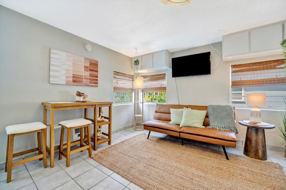 Settle into your inviting living space with cozy leather seating, natural textures, and warm wood tones. Sunlight streams through bamboo shades as you enjoy your morning coffee at the bistro table.