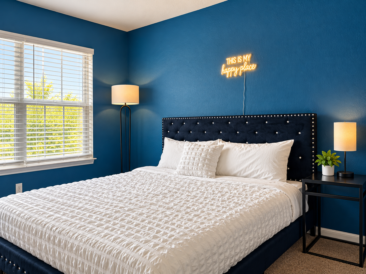 Your serene bedroom sanctuary features rich blue walls and a plush bed with a tufted headboard, bathed in natural light from a large window overlooking greenery.