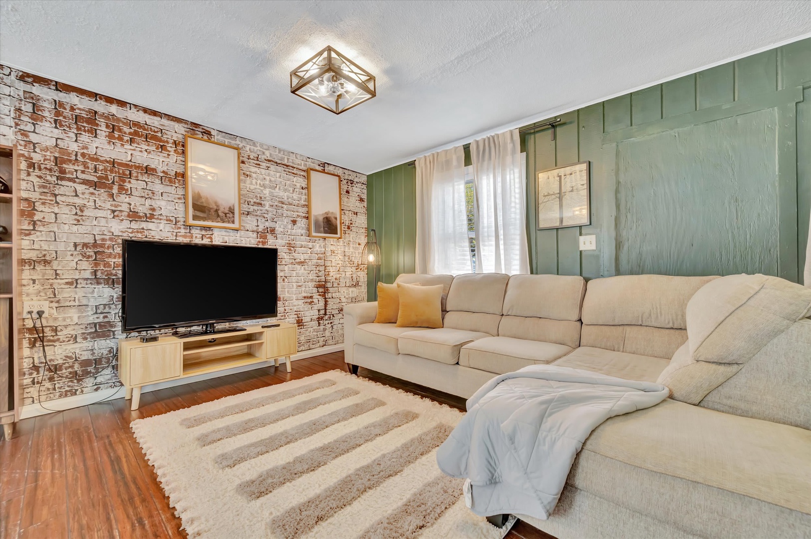 Unwind on plush sectional seating where rustic exposed brick meets calming sage paneling, creating your perfect retreat for movie nights and lazy afternoons.