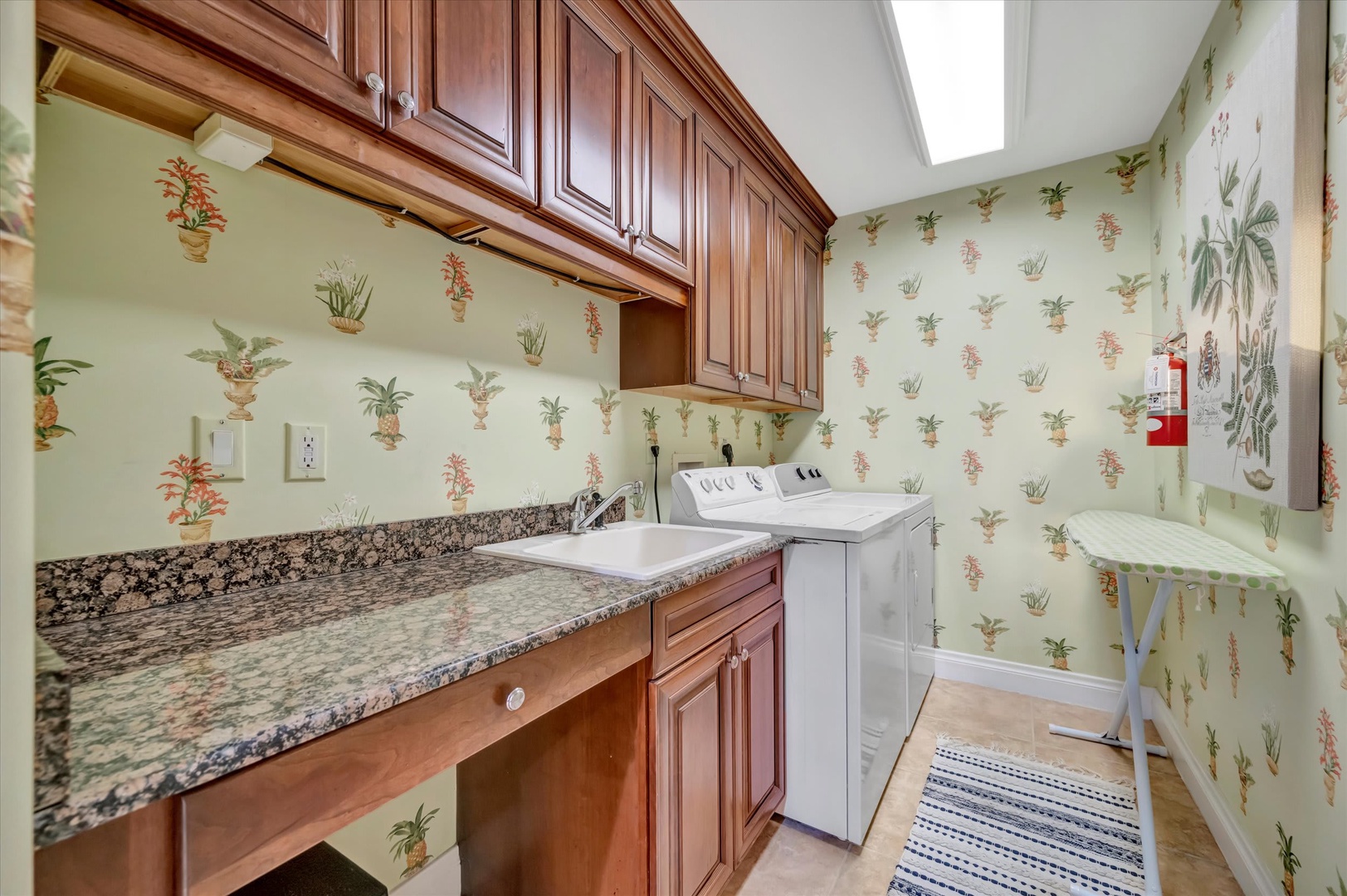 Your laundry routine gets an upgrade in this bright, charming space with rich wood cabinetry, granite countertops, and cheerful tropical wallpaper that makes chores feel less like work.