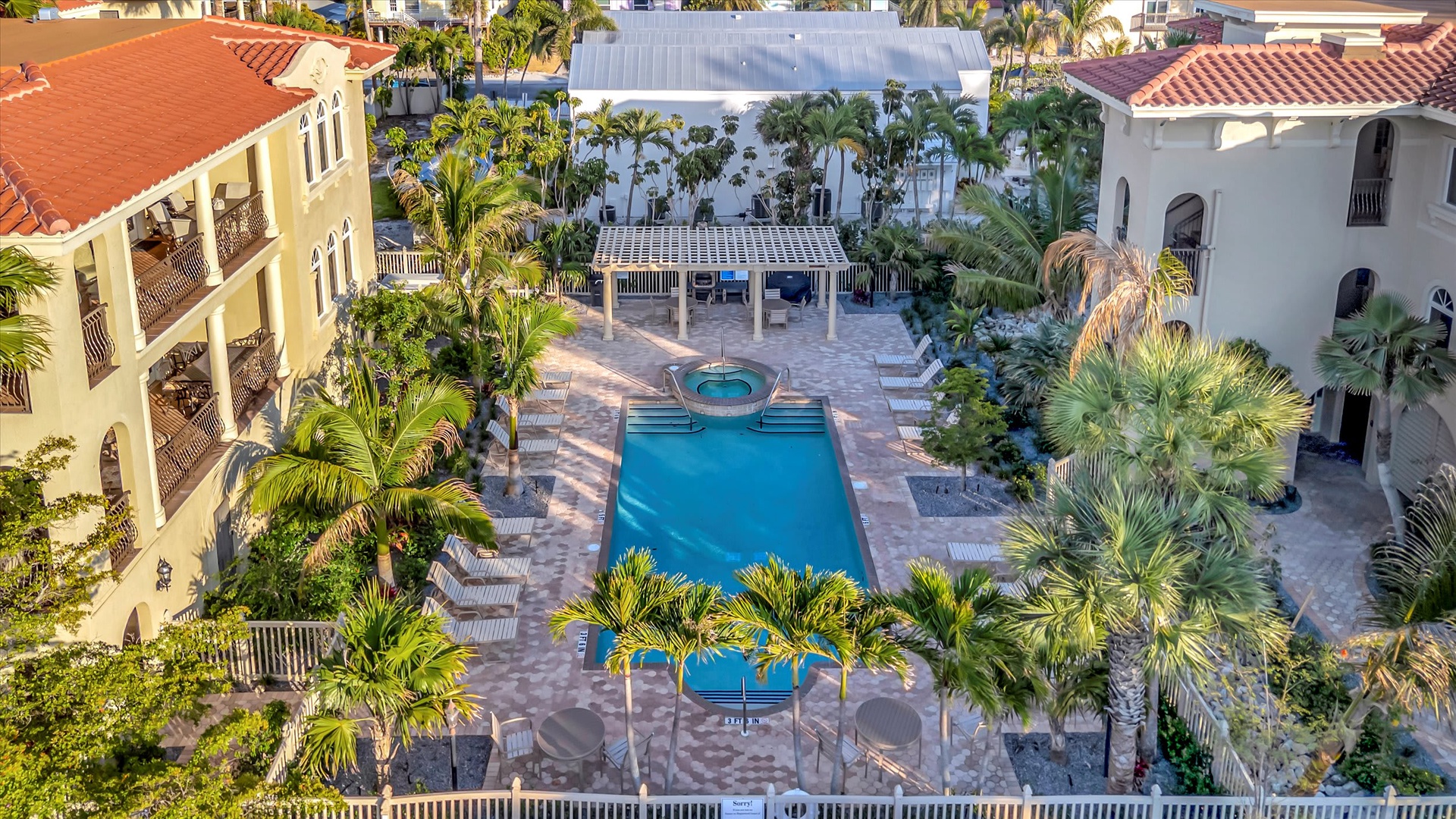 Aerial view of the property showcasing a lush tropical courtyard with central pool, surrounded by colorful Mediterranean-style buildings and abundant palm trees.