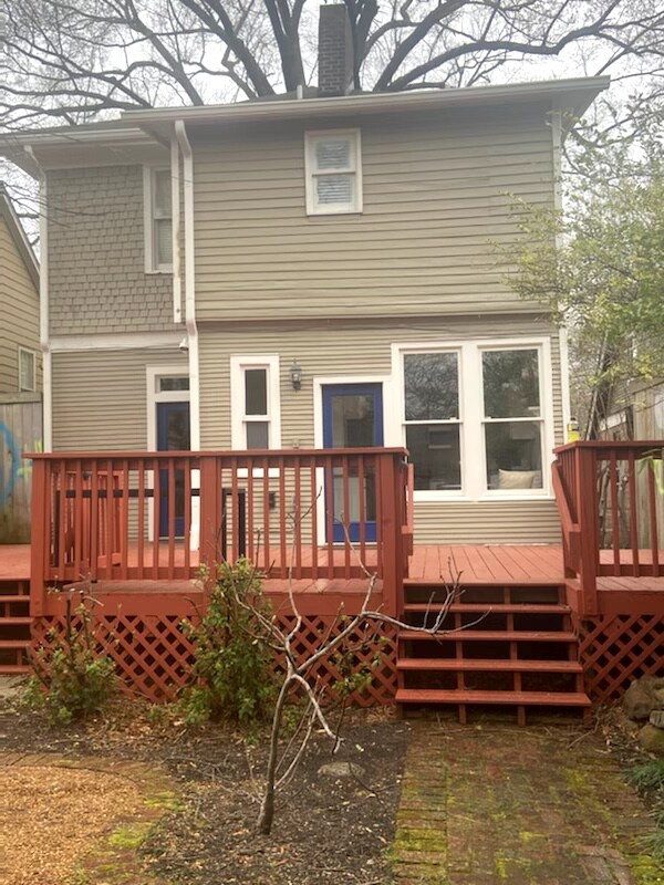 A charming two-story vacation rental with a welcoming red deck, perfect for morning coffee or evening relaxation. The spacious outdoor area blends seamlessly with the quiet, tree-lined setting.