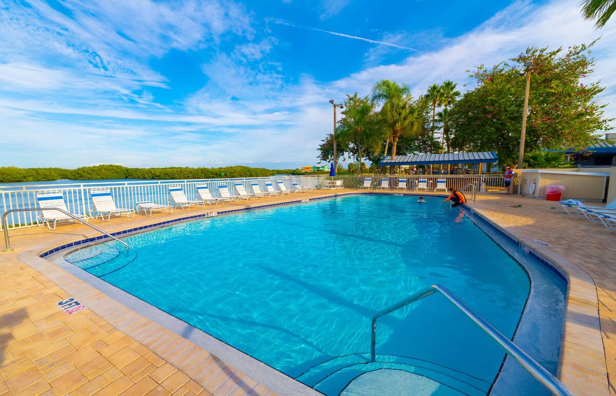 Waterside pool area surrounded by lush tropical landscaping, where you can unwind on lounge chairs with views stretching over calm natural waters.