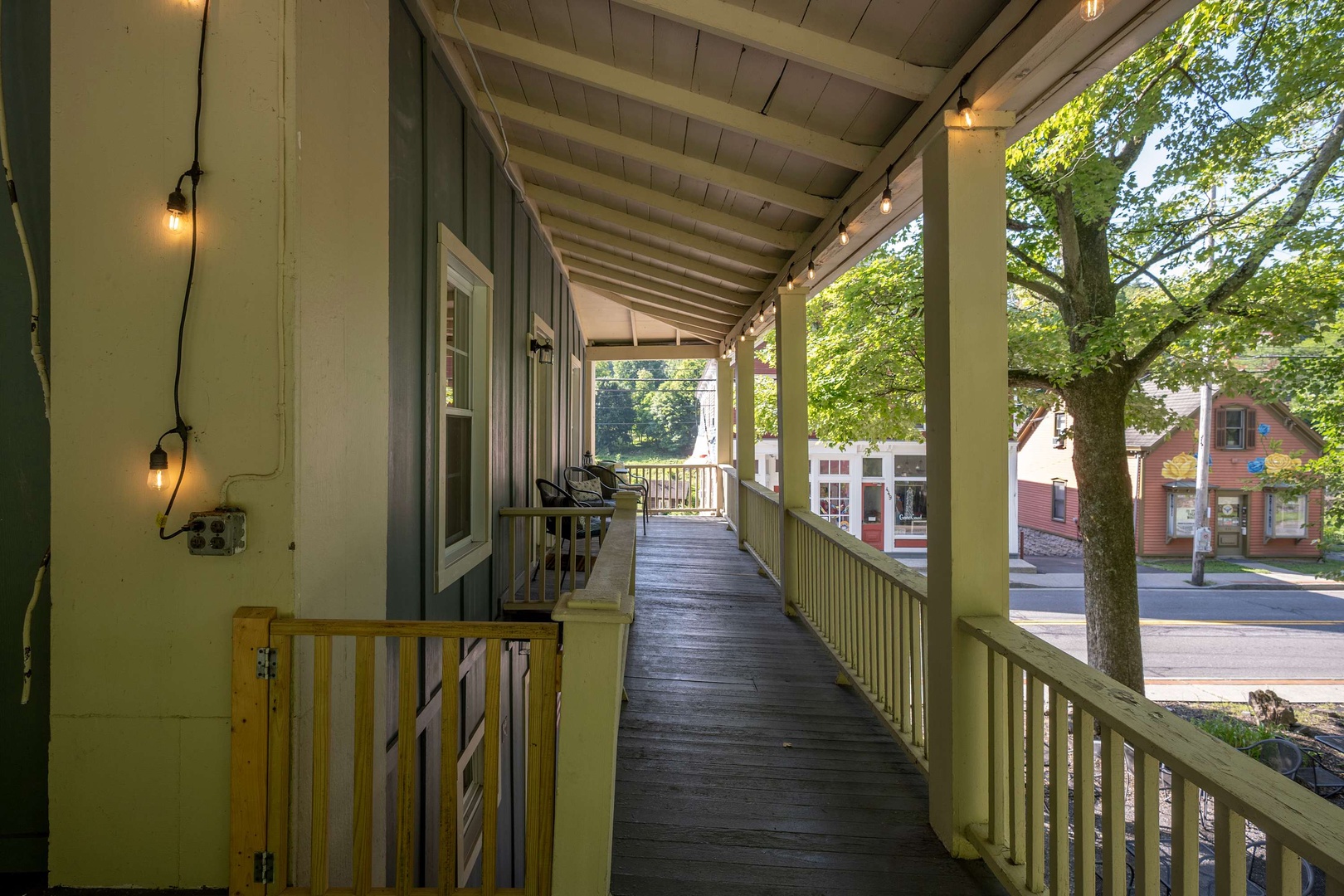 The covered porch wraps around the property, offering a quiet place to unwind as warm string lights glow overhead and tree-lined streets set a peaceful scene beyond the railing.