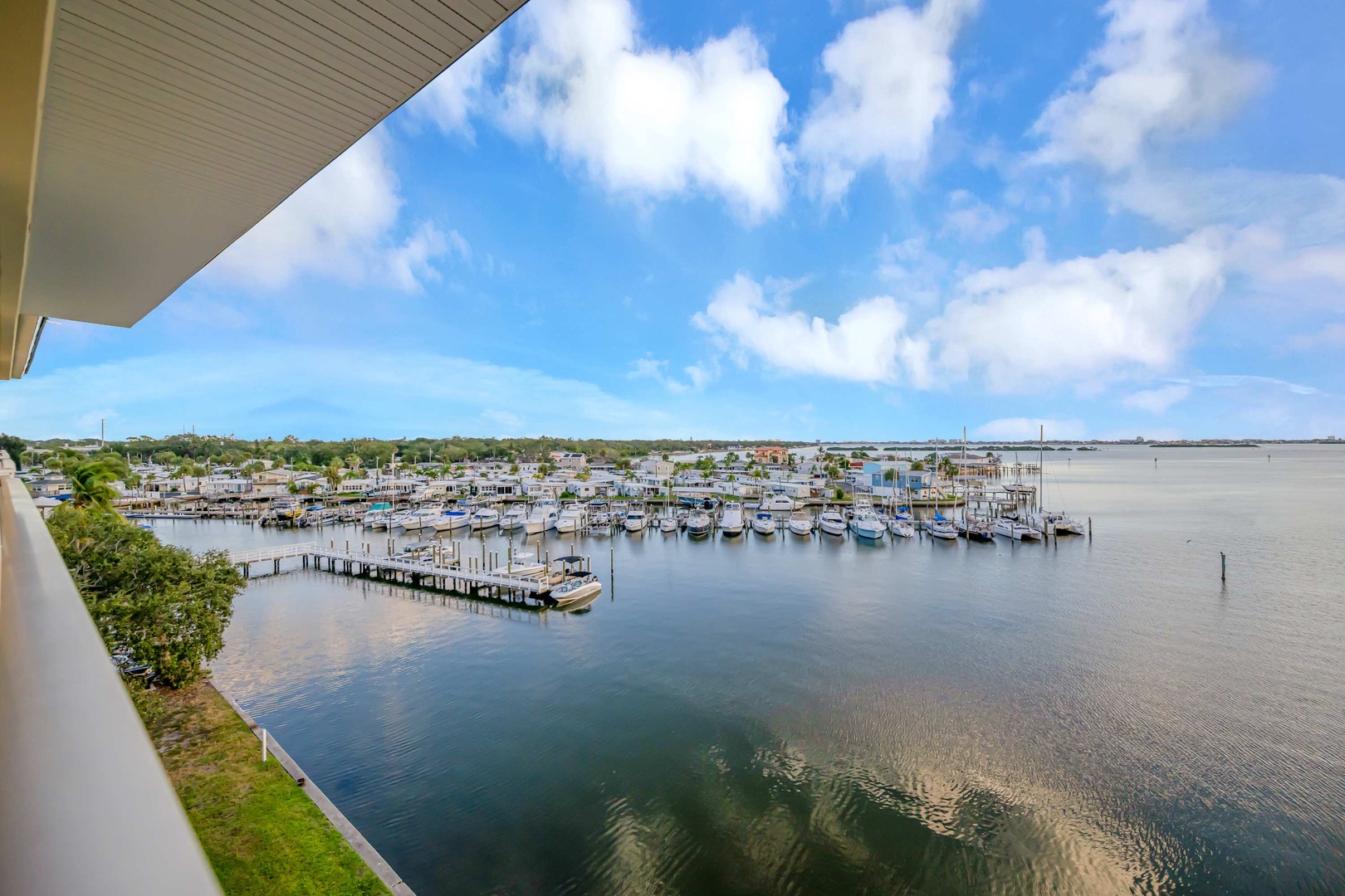 Marina views overlooking docked boats and calm waterways, framed by a bright blue sky and distant coastal homes.