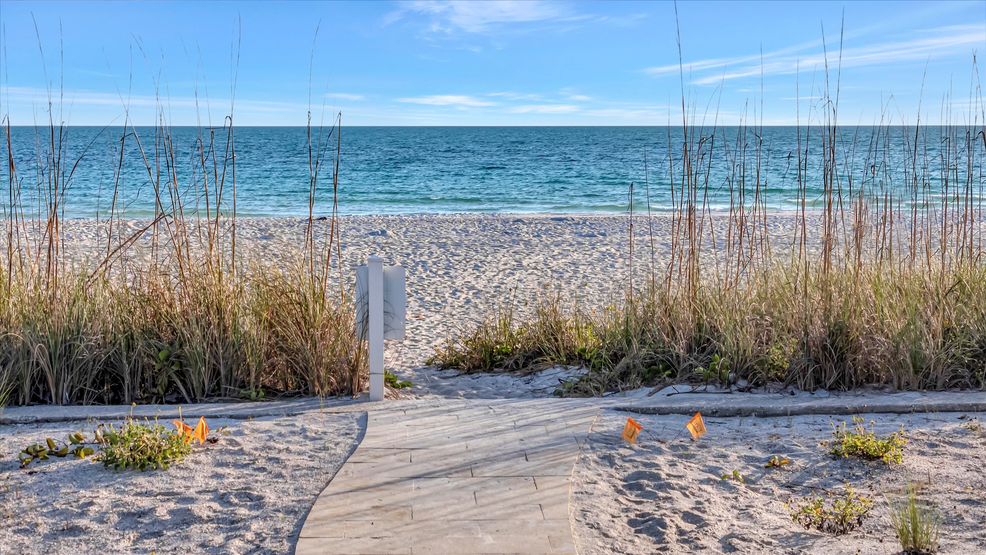 A private boardwalk leads through coastal dunes straight to powdery sand and turquoise waters, where gentle waves and endless horizon create your perfect beachside escape.