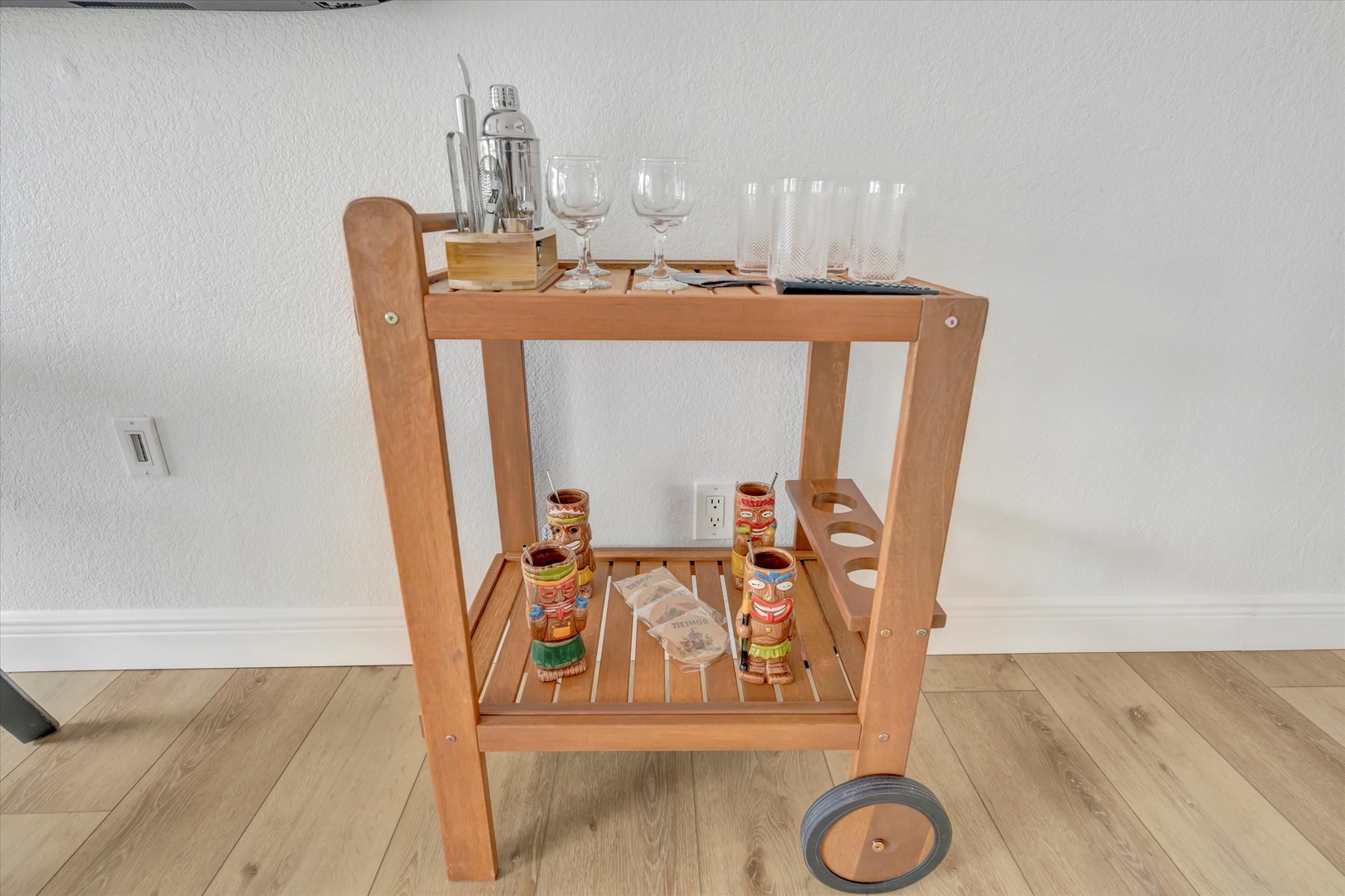Mix your favorite cocktails with ease at your stylish bar cart, stocked with glasses, shaker, and tiki mugs—everything you need for a relaxing evening at home.