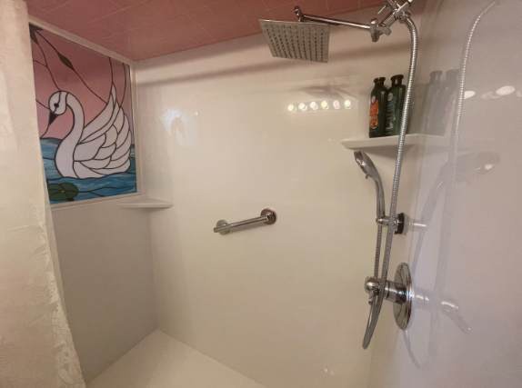 Step into a bright, spotless shower with modern fixtures and a convenient grab bar. The built-in shelf and playful window detail add charm to your daily routine.
