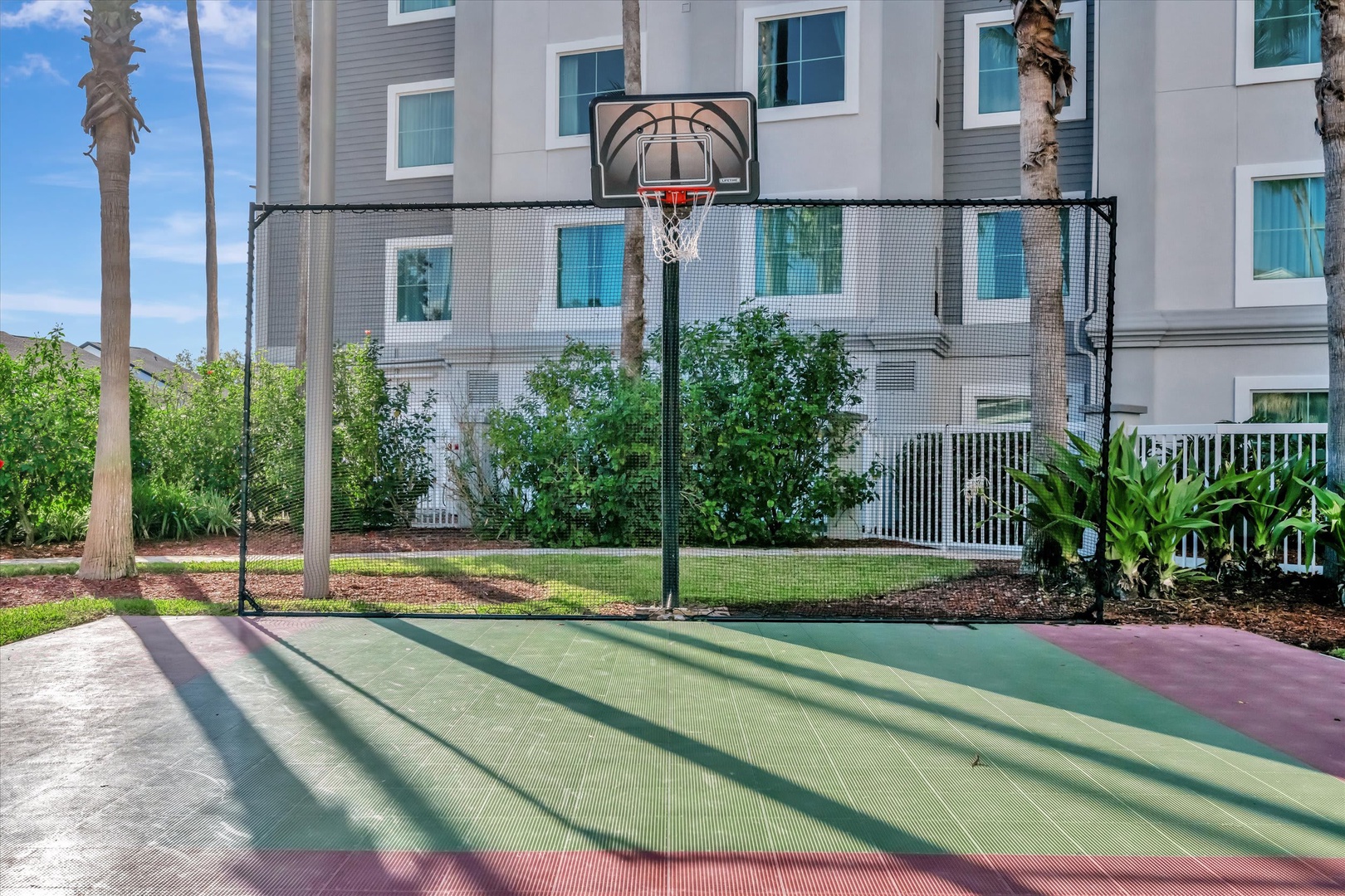 Outdoor basketball court with protective netting, perfect for friendly games under sunny skies. The property building and lush landscaping create a welcoming backdrop for active moments.