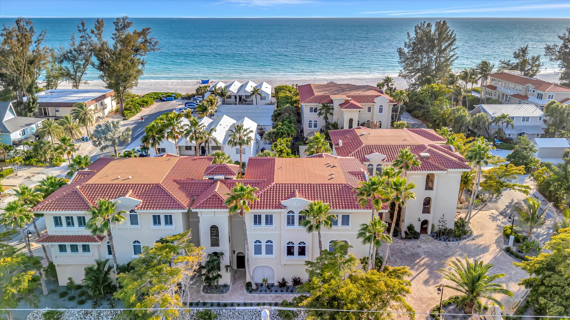 Beachfront property nestled along a pristine shoreline, featuring red tile roofs, lush tropical landscaping, and immediate access to white sand and turquoise waters.