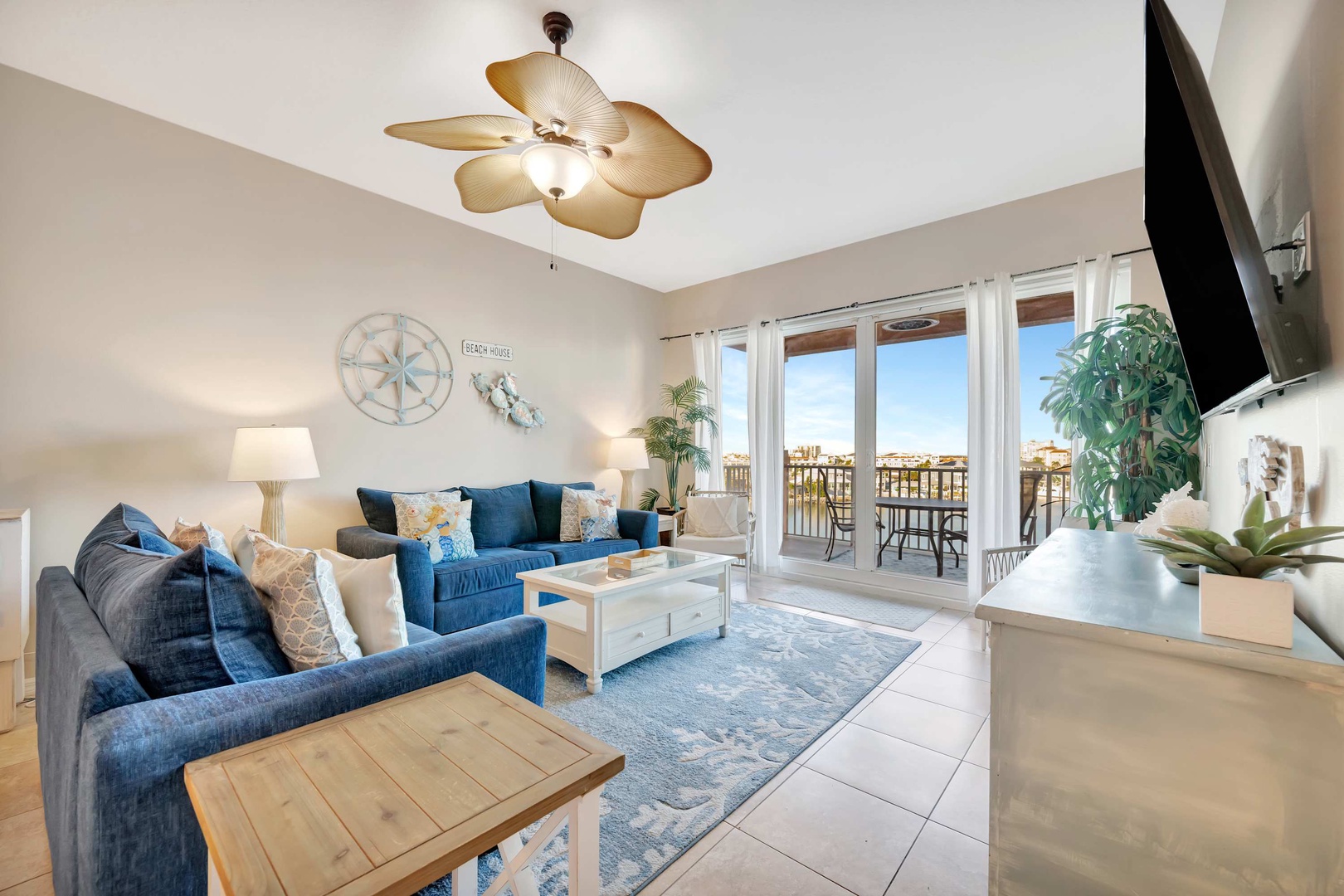 Unwind in this coastal-inspired living room with plush seating, breezy ceiling fan, and tropical accents. Your beachside retreat awaits just beyond those glass doors.