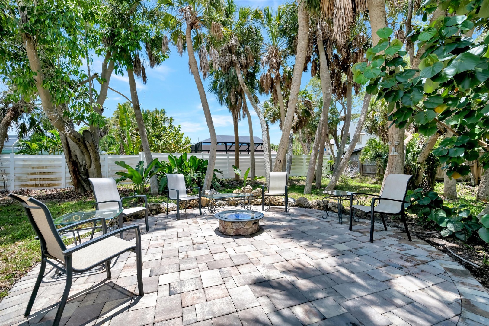 Your private patio oasis awaits, with shaded seating circling a fire pit beneath tall palms—perfect for relaxing mornings or cozy evening gatherings under the Florida sky.