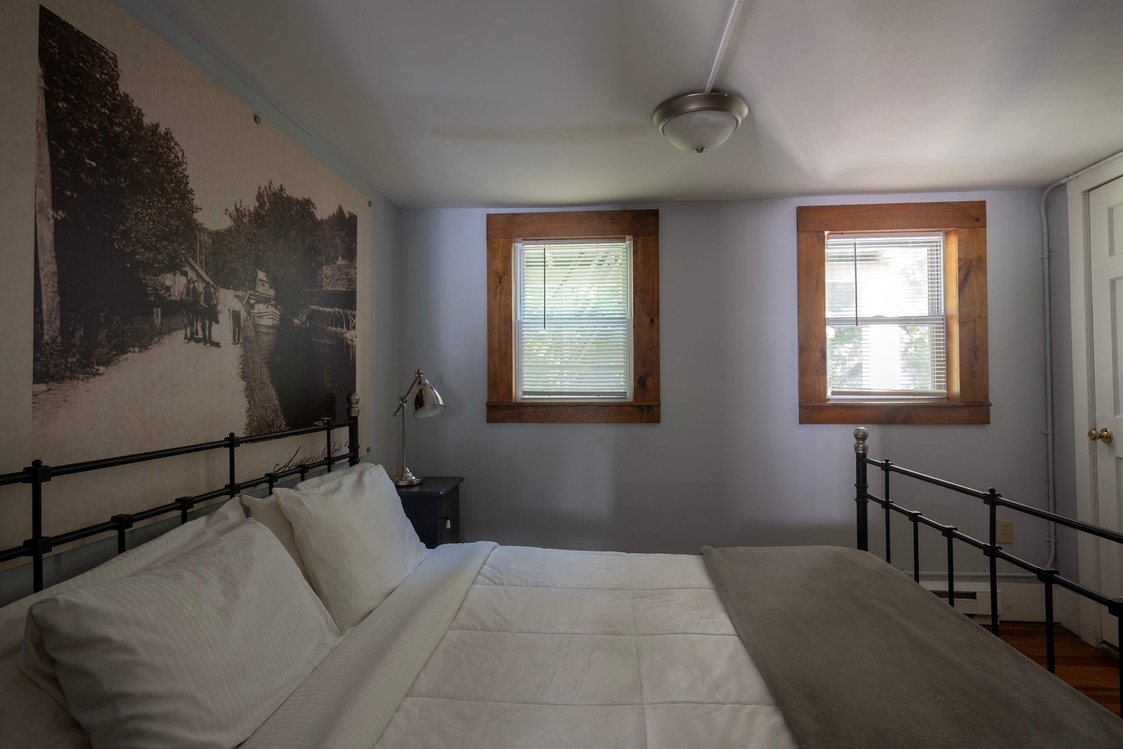 Rest peacefully in your serene bedroom with a cozy bed framed by rustic wood-trimmed windows and calming blue walls adorned with vintage artwork.
