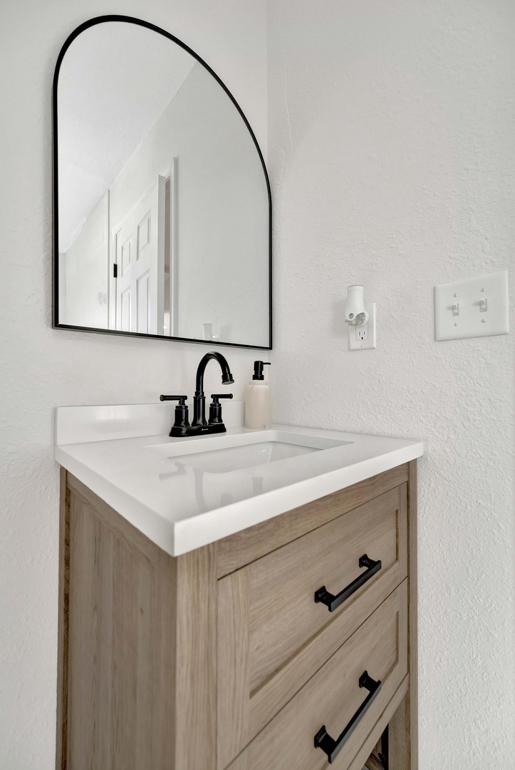 Step into your modern bathroom retreat featuring a sleek vanity with warm wood tones and crisp white countertops. The stylish arch mirror and matte black fixtures create a contemporary sanctuary where you can refresh and unwind.