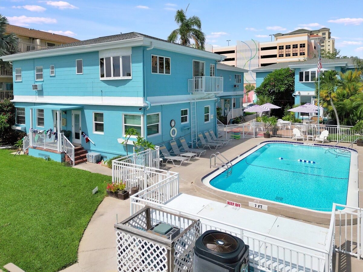 A cheerful turquoise beach house with inviting pool and lounge area, surrounded by lush tropical palms and sunny Florida skies—perfect for relaxed coastal getaways.