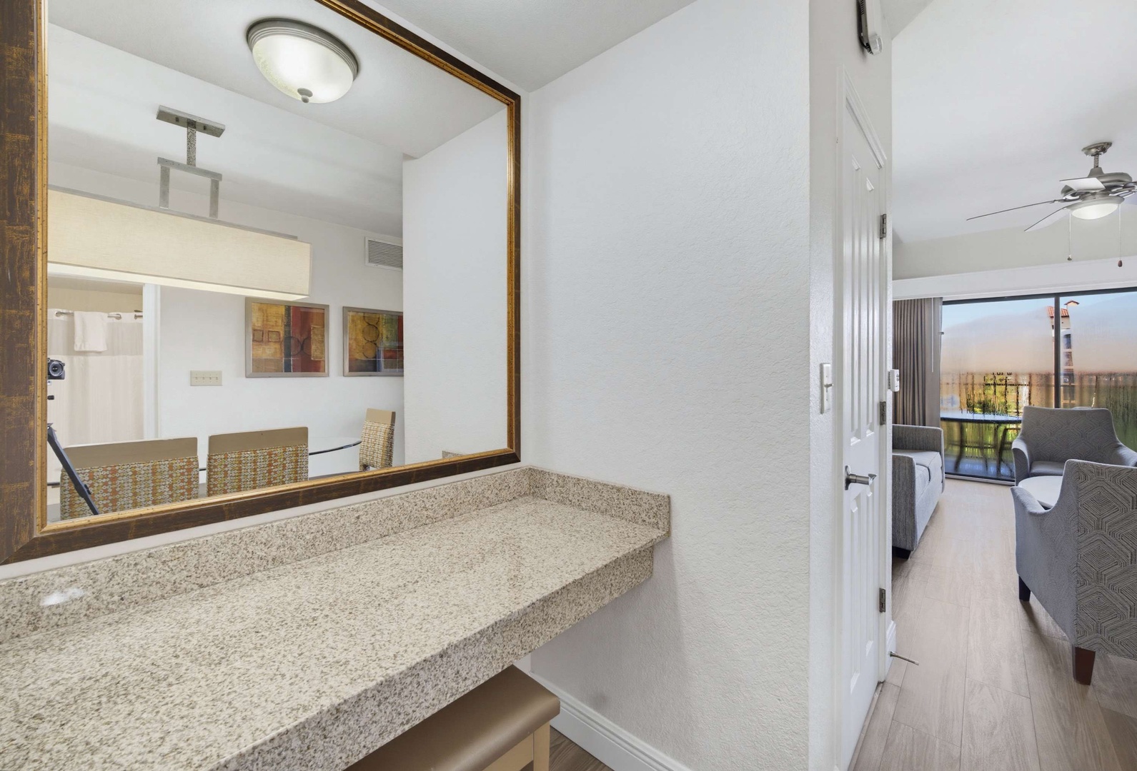 Freshen up at the vanity area with a granite countertop and ample lighting, just steps from your cozy living space and private balcony beyond.
