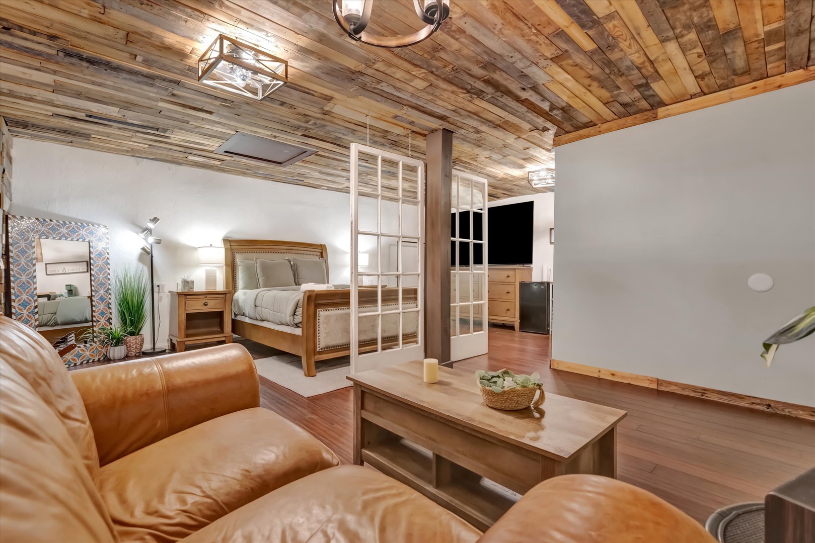 Relax in your open-concept space where rustic wood beams and stylish glass dividers create a warm, inviting retreat. Sink into the plush leather sofa or unwind in your cozy bedroom nook—this charming studio blends comfort and character perfectly.
