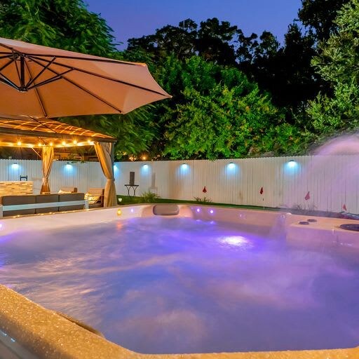 This twilight-lit pool area features atmospheric purple lighting, a shaded poolside lounge, and a serene private courtyard surrounded by lush greenery—perfect for unwinding under the stars.