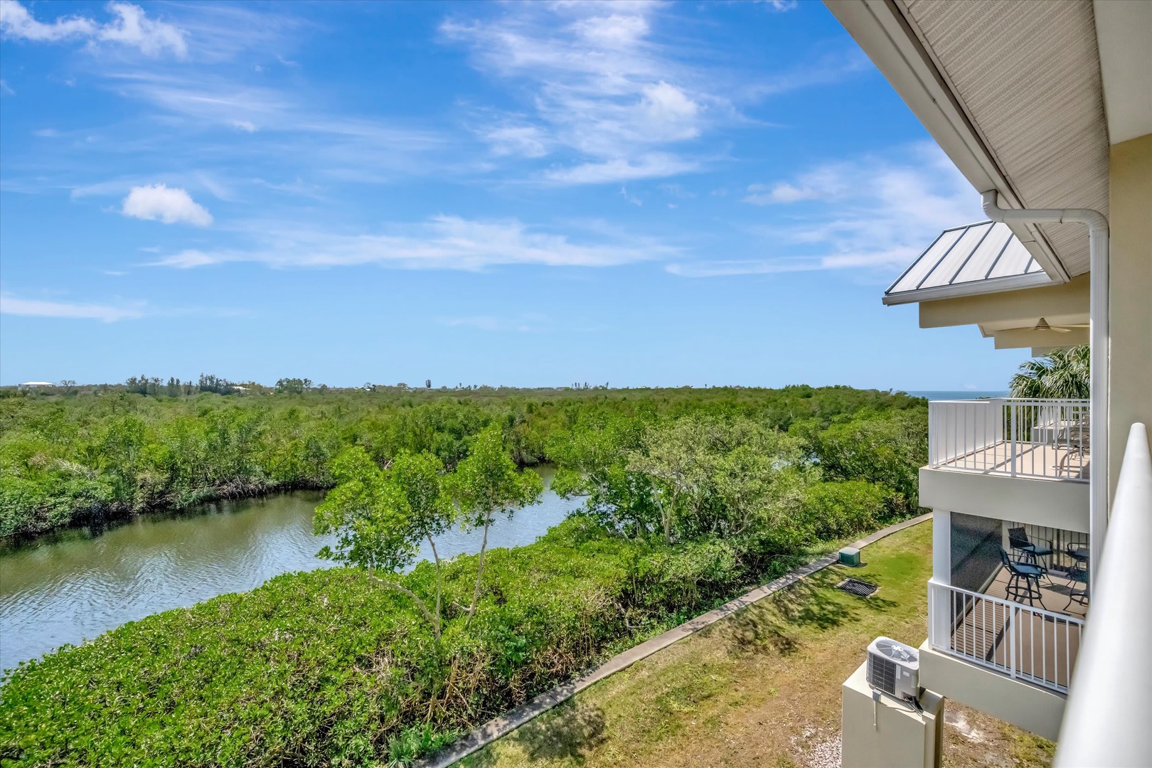 The property overlooks a peaceful river winding through lush mangroves, with glimpses of the ocean in the distance under a bright blue sky.