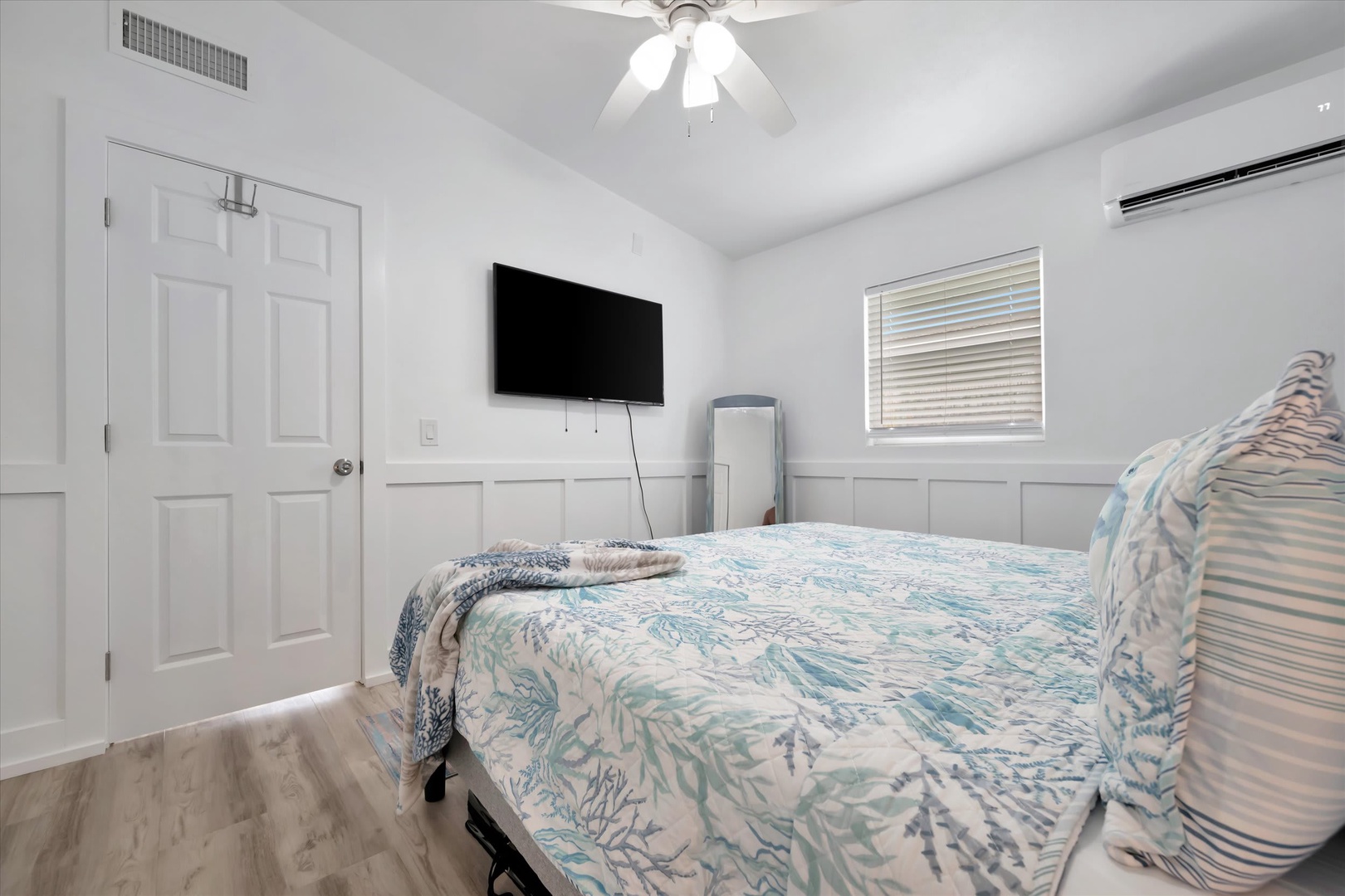 Your bright coastal bedroom features high ceilings with a fan, crisp white walls with wainscoting, and a plush bed dressed in soothing aqua tones—perfect for restful nights.