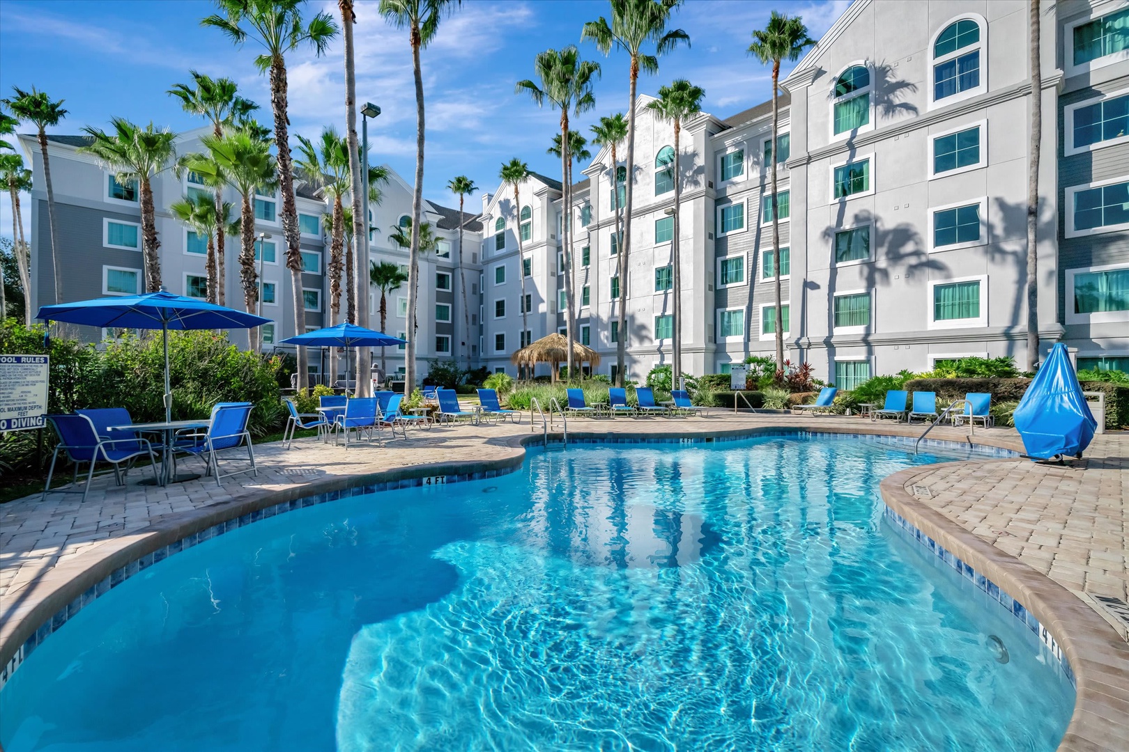 A sparkling pool surrounded by swaying palms invites you to unwind under the warm sunshine, with plenty of lounge chairs and umbrellas ready for your perfect poolside afternoon.