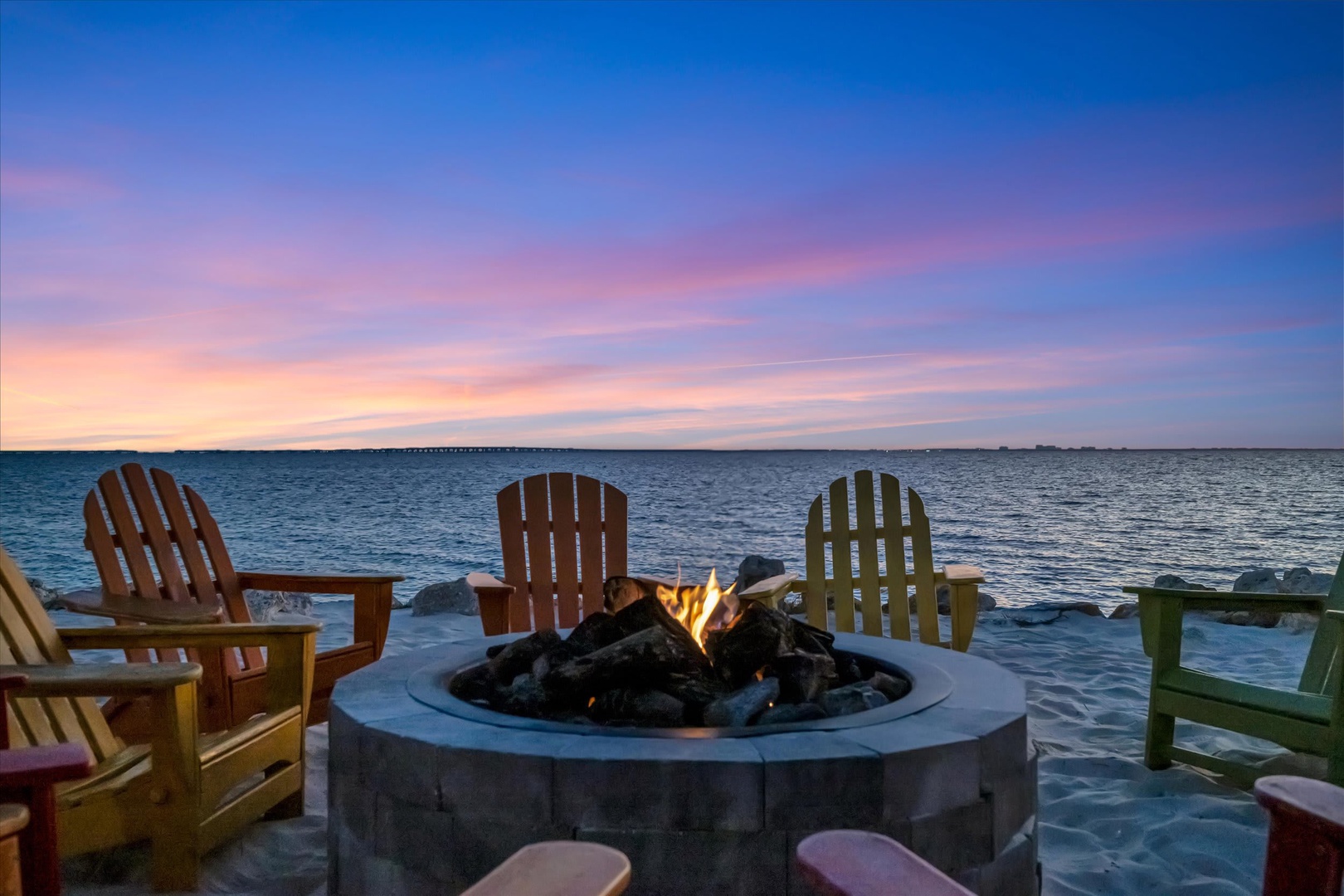 A crackling fire pit awaits you right on the shore, surrounded by colorful Adirondack chairs and endless water views. Watch the sky blush pink and gold as evening settles over the bay.