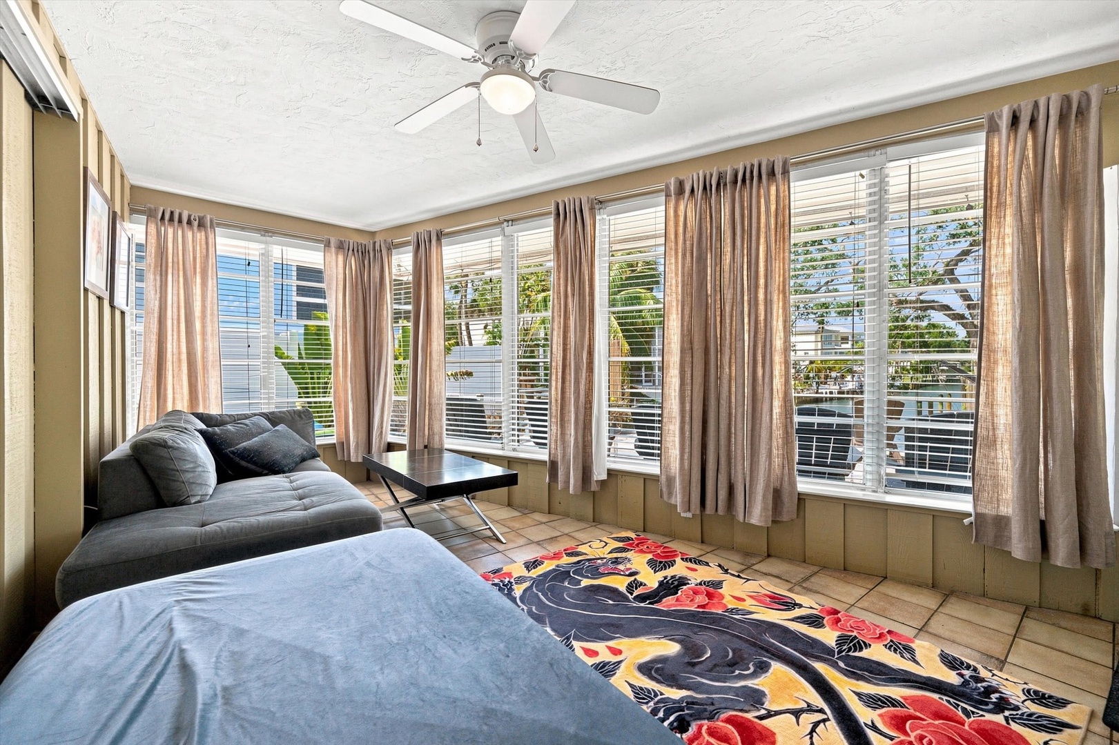 Settle into this bright, airy living space with plenty of natural light streaming through multiple windows. The ceiling fan keeps things cool while you relax on the cozy sectional sofa.