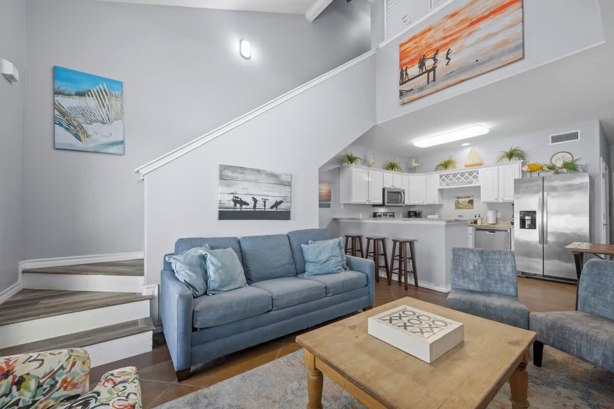 Unwind in your airy, coastal-inspired living space with soaring ceilings, a comfy sofa perfect for evening relaxation, and an open kitchen ready for your culinary adventures.