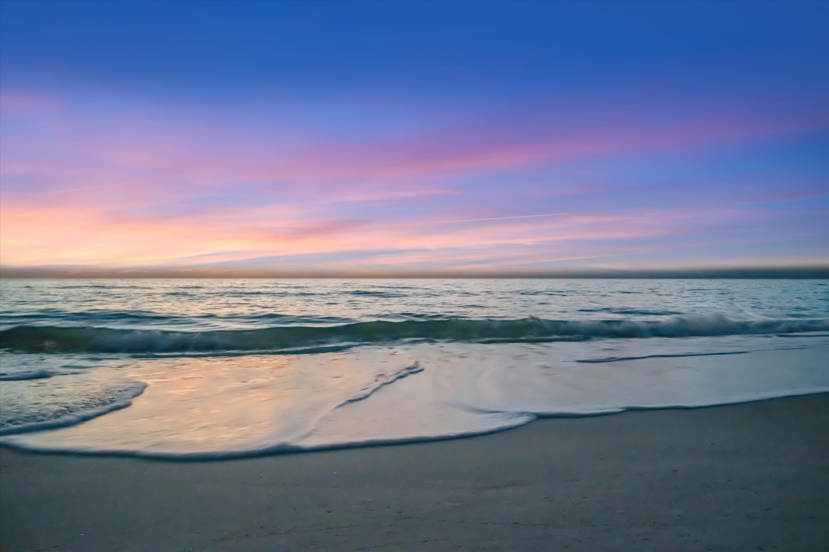 The property sits near a tranquil beach where gentle waves meet soft sand beneath pastel skies at dawn.
