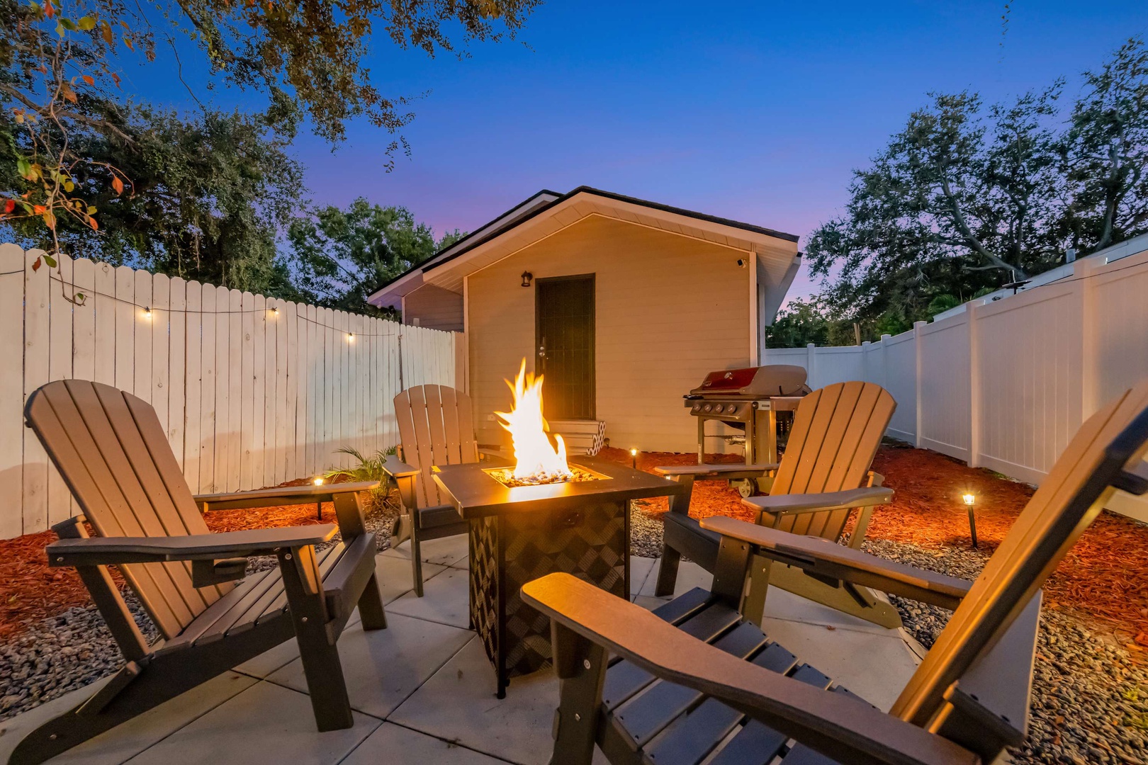 Gather around the fire pit as twilight paints the sky, roasting marshmallows and sharing stories while the grill stands ready for your cookout under softly glowing lights.