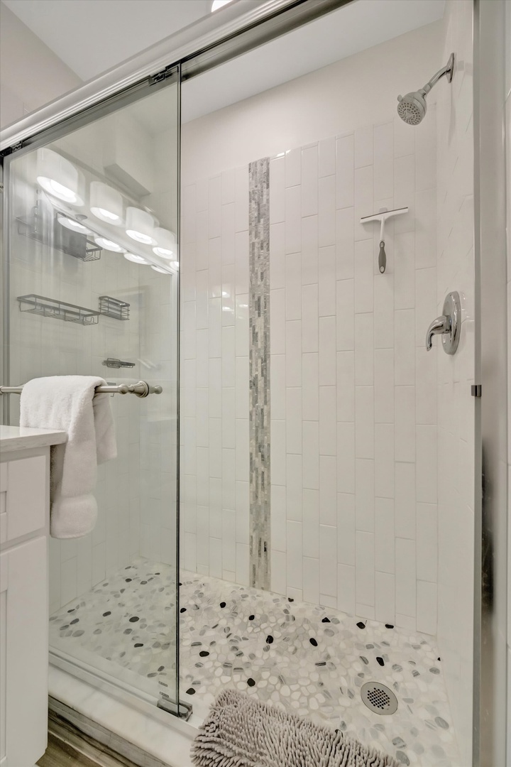 Step into this bright, immaculate shower where sleek white tiles and soothing mosaic accents create your personal spa retreat.