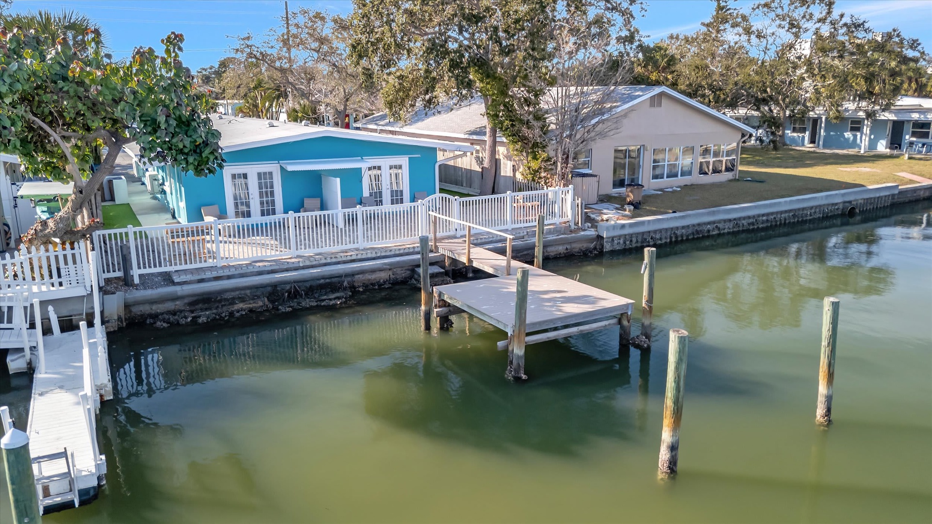 Waterfront cottages with private docks line a peaceful canal, framed by mature trees and clear skies in this quiet coastal neighborhood.
