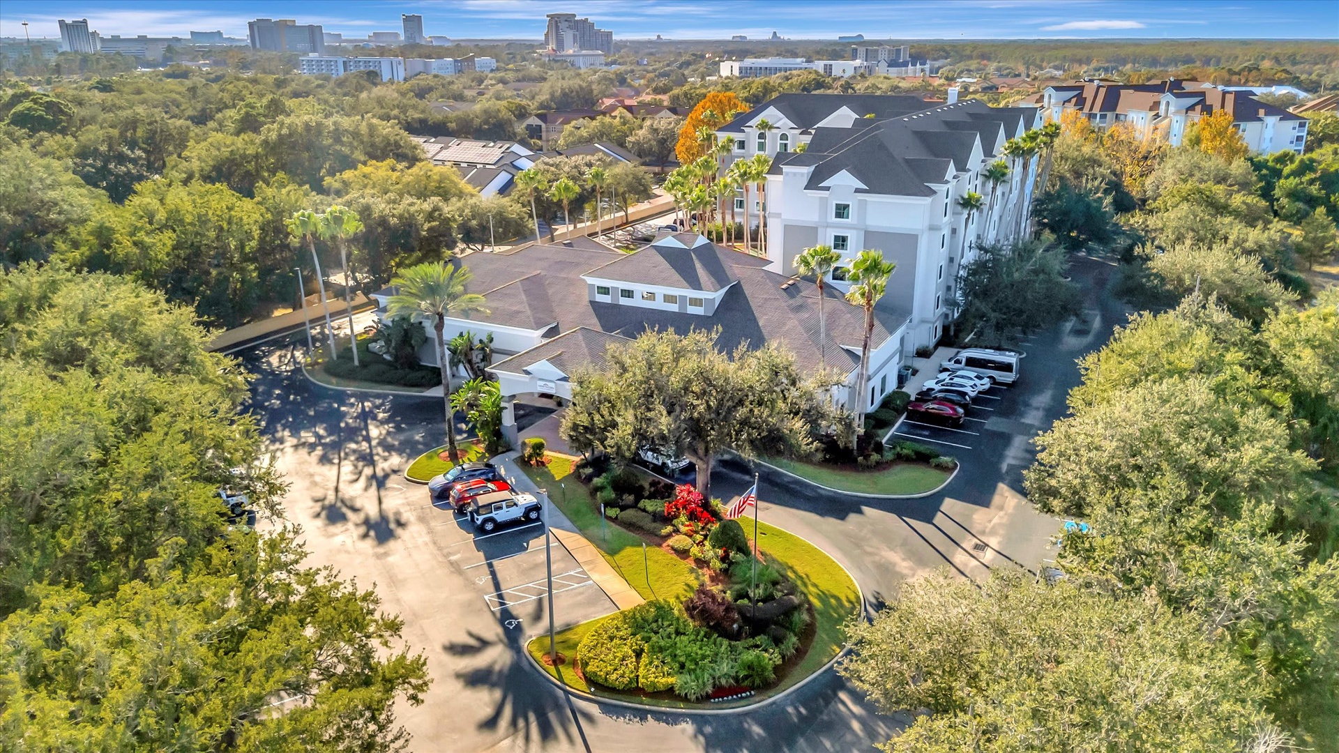 Aerial view of the property entrance and surrounding parklike grounds, with mature trees and landscaped gardens framing the building in a peaceful setting near downtown.