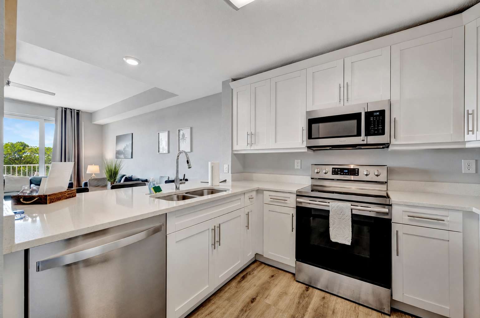 Bright modern kitchen with sleek white cabinetry, quartz countertops, and stainless steel appliances. Natural light floods through the skylight, with direct access to a peaceful balcony.