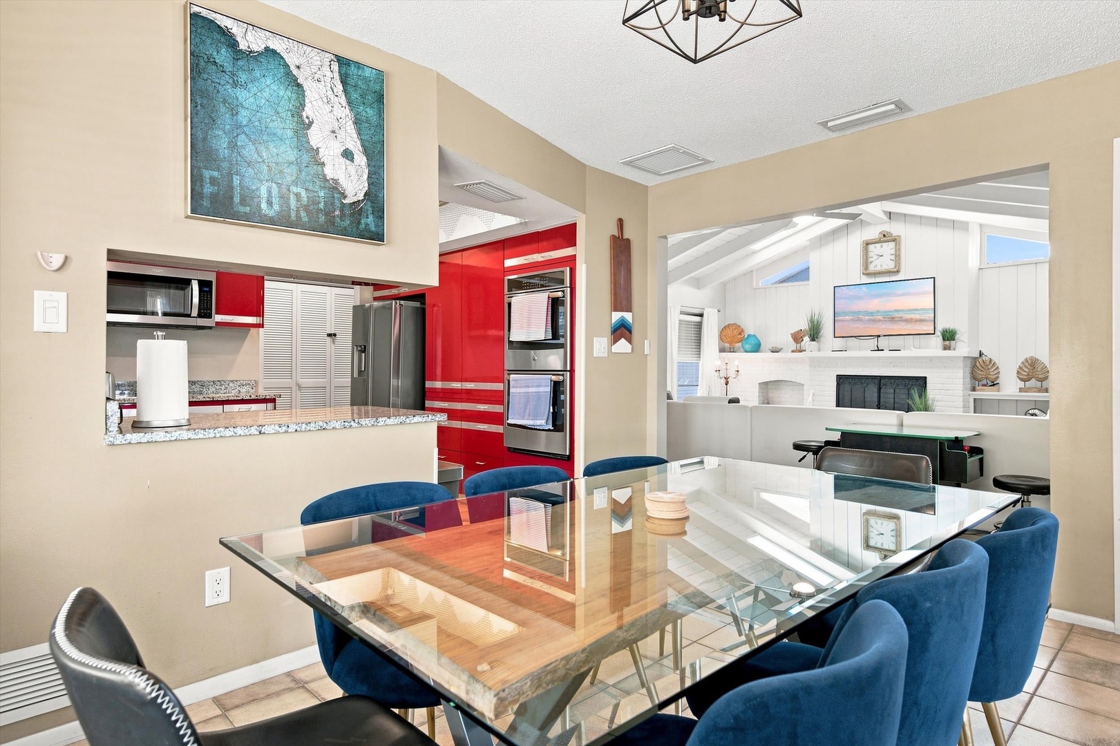 Bright, modern space with sleek dining and bold red kitchen accents. A scenic framed map adds coastal charm overhead, while natural light flows through the open layout.